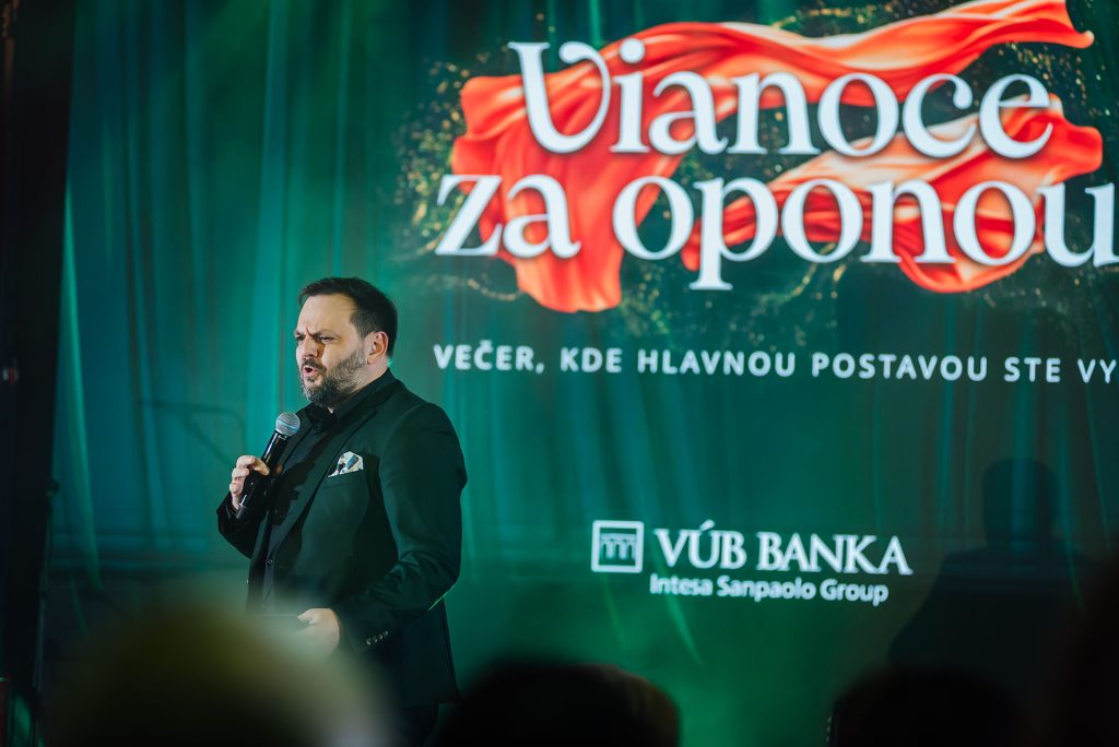Moderátor na pódiu pod nápisom Vianoce za oponou, Večer, kde hlavnou postavou ste vy