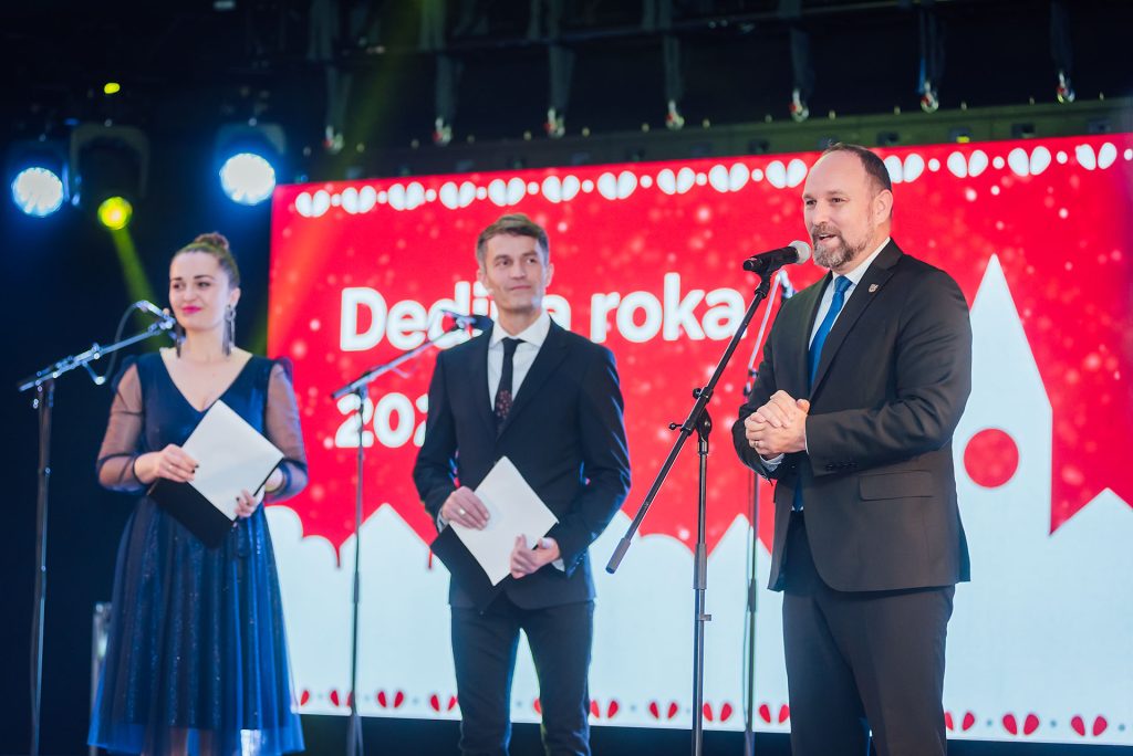 Moderátori a hosť na pódiu pred obrazovkou Dedina roka 2025