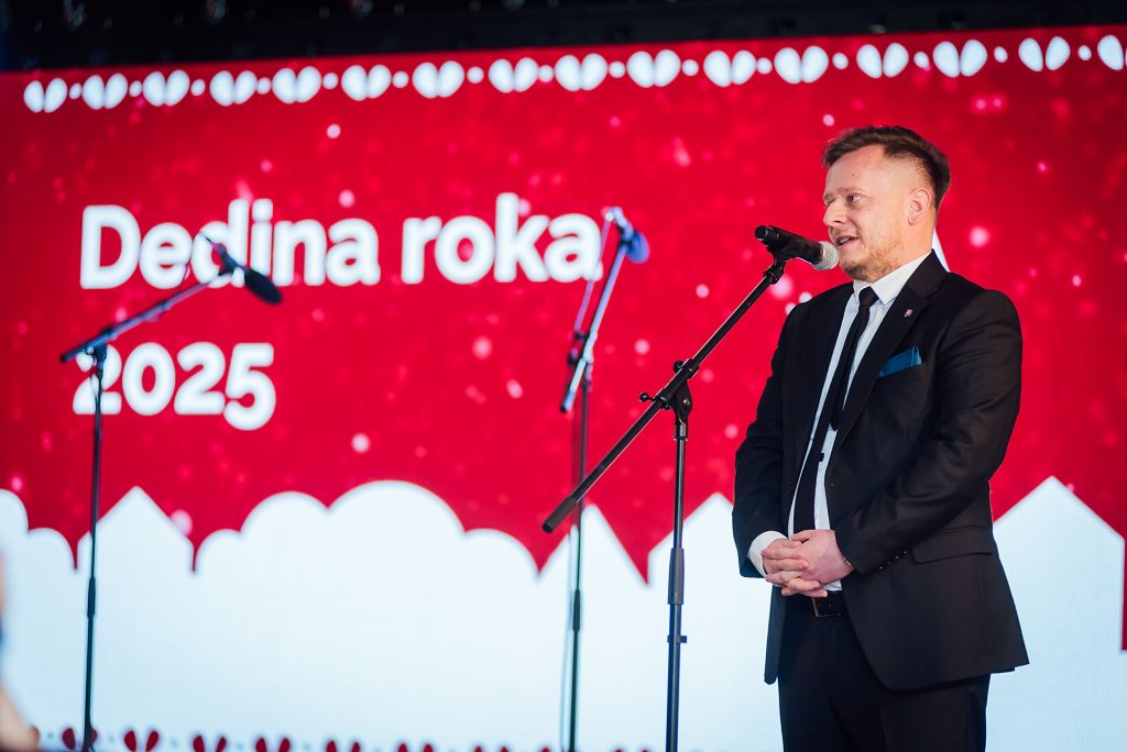 Rečník pri mikrofóne pred obrazovkou s nápisom Dedina roka 2025
